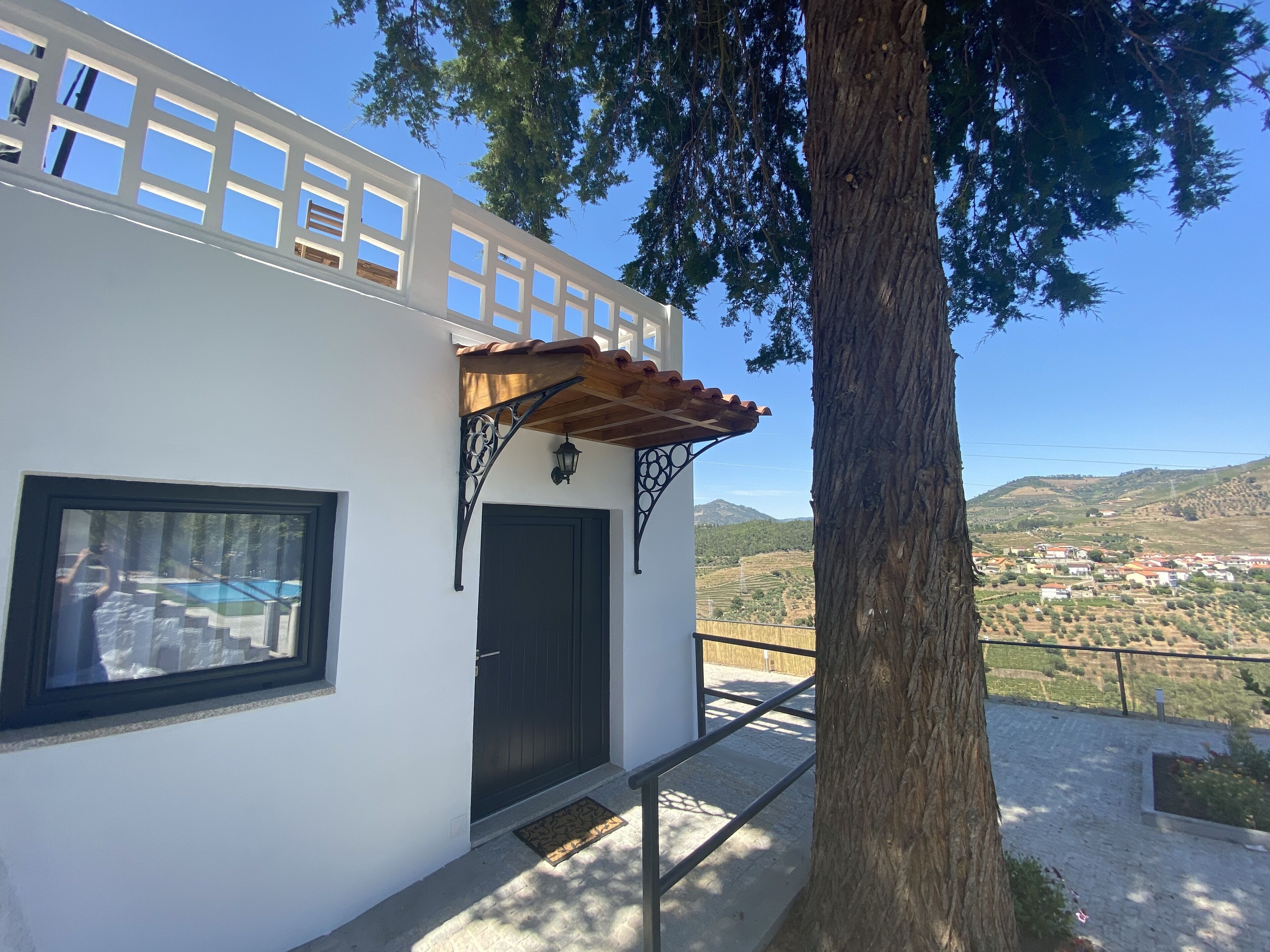 Il s’agit d’un bâtiment à l’extérieur blanc, avec une porte noire et une fenêtre. Un arbre se trouve devant le bâtiment.
