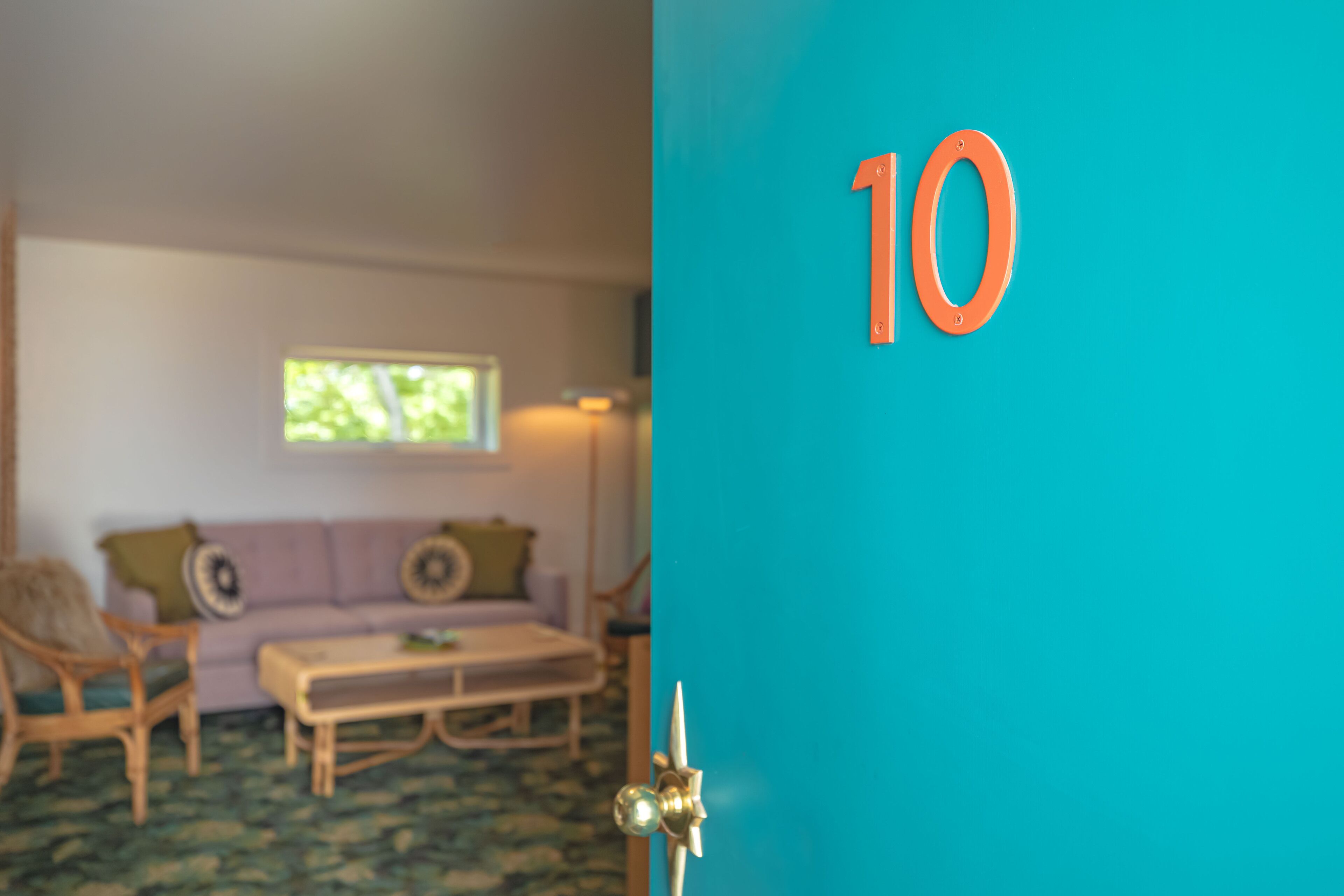 A room with a teal door, a wooden bench, a purple sofa, and a window with a view of trees.