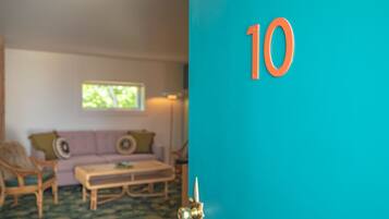 A room with a teal door, a wooden bench, a purple sofa, and a window with a view of trees.