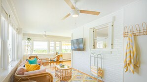 A bright living room with a ceiling fan, wicker furniture, a patterned rug, and a television on the wall. - Rye Motor Inn - Oceanfront, Walk to Beach (Rye)