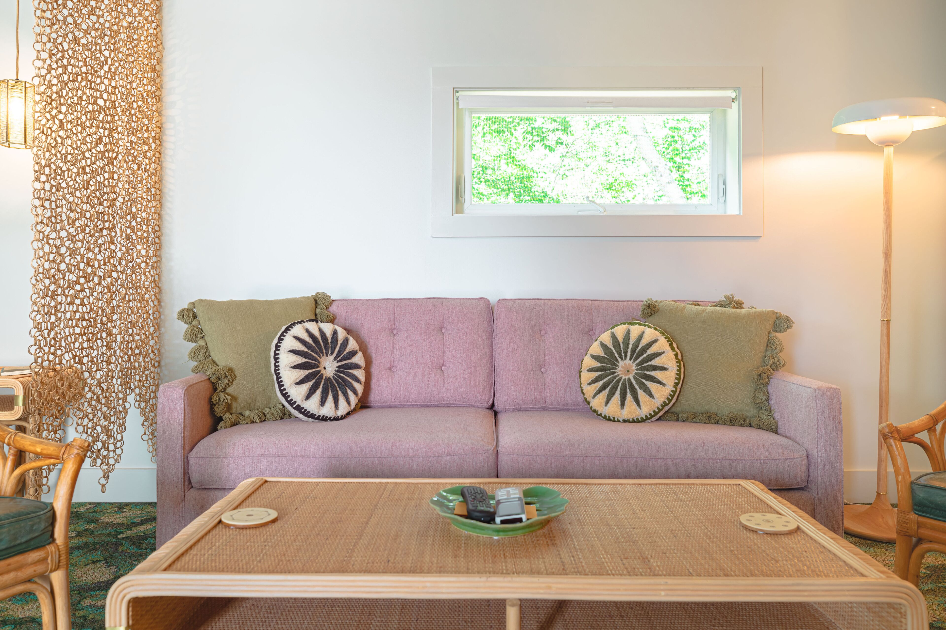 Un salon avec un canapé violet, deux coussins décoratifs, une table basse en osier et un lampadaire.