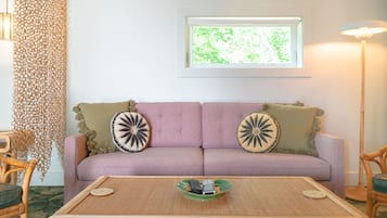 Un salon avec un canapé violet, deux coussins décoratifs, une table basse en osier et un lampadaire.