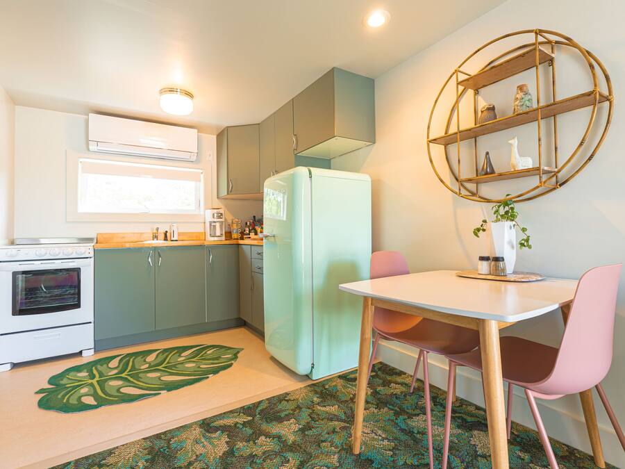 Een kleine keuken met een koelkast, oven en een eethoek met een tafel en stoelen.