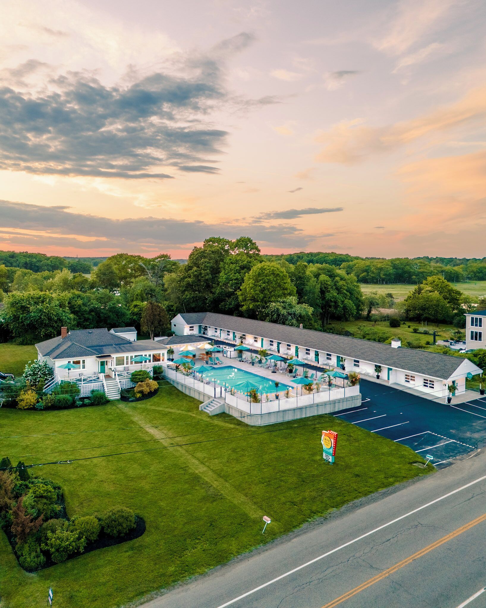 A hotel with a swimming pool, a parking lot, and a road in the foreground.