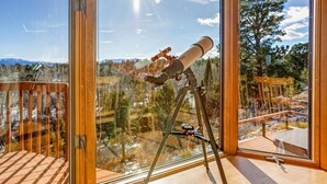 A telescope on a tripod inside a room with large windows overlooking a mountainous landscape. - Stargazer Retreat • Hot Tub•Game Room• Creek Walk•DogFriendly• 360° Mtn Views (Nathrop)