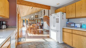 A modern kitchen with wooden cabinets, a white refrigerator, and a dining area with a wooden table and chairs. - Stargazer Retreat • Hot Tub•Game Room• Creek Walk•DogFriendly• 360° Mtn Views (Nathrop)