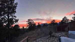 A hot tub on a wooden deck with a view of a sunset and mountains. - Stargazer Retreat • Hot Tub•Game Room• Creek Walk•DogFriendly• 360° Mtn Views (Nathrop)