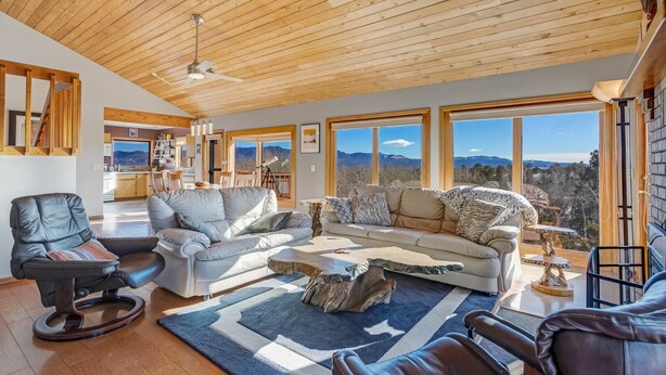 A spacious living room with a high wooden ceiling, large windows offering mountain views, and a cozy seating area with leather chairs and sofas. - Stargazer Retreat • Hot Tub  •Game Room• Creek Walk•DogFriendly• 360° Mtn Views (Nathrop)