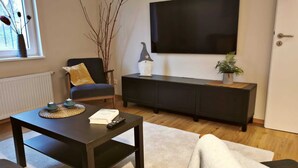 A modern living room with a dark wooden coffee table, a sofa, a black entertainment unit, and a large flat-screen TV mounted on the wall. - Little house on the historic city wall (Höxter)