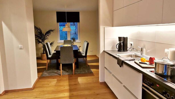 A modern kitchen with white cabinets, a black stove, and a dining area with a table and chairs. - Little house on the historic city wall (Höxter)