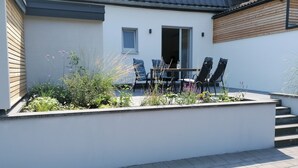 A modern outdoor patio with a table and chairs, surrounded by a low wall and plants. - Little house on the historic city wall (Höxter)