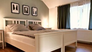A bedroom with a white bed, a nightstand, a lamp, and a window with curtains. - Little house on the historic city wall (Höxter)