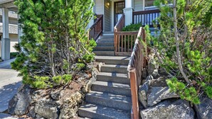 Un bâtiment doté d’un escalier en pierre menant à une porte en bois, le tout entouré de pins.