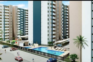 Edifício residencial alto com várias varandas, piscina e área de estacionamento.