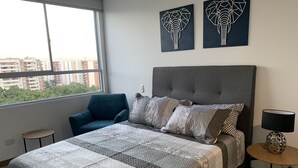 A modern bedroom with a large bed, a blue armchair, and two elephant-themed wall art pieces. - Executive apartment (Cali)