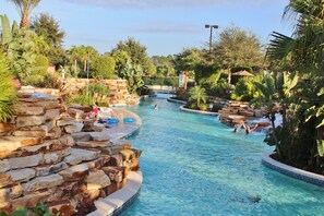 A swimming pool with a waterfall feature, surrounded by tropical vegetation and stone walls.