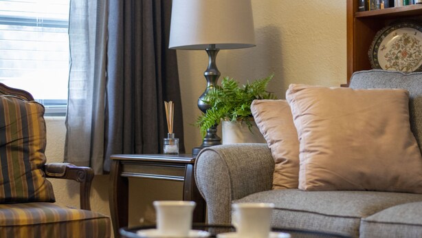 Ein gemütliches Wohnzimmer mit einer Couch, einem Sessel, einer Lampe und einem Tablett mit Tassen.
