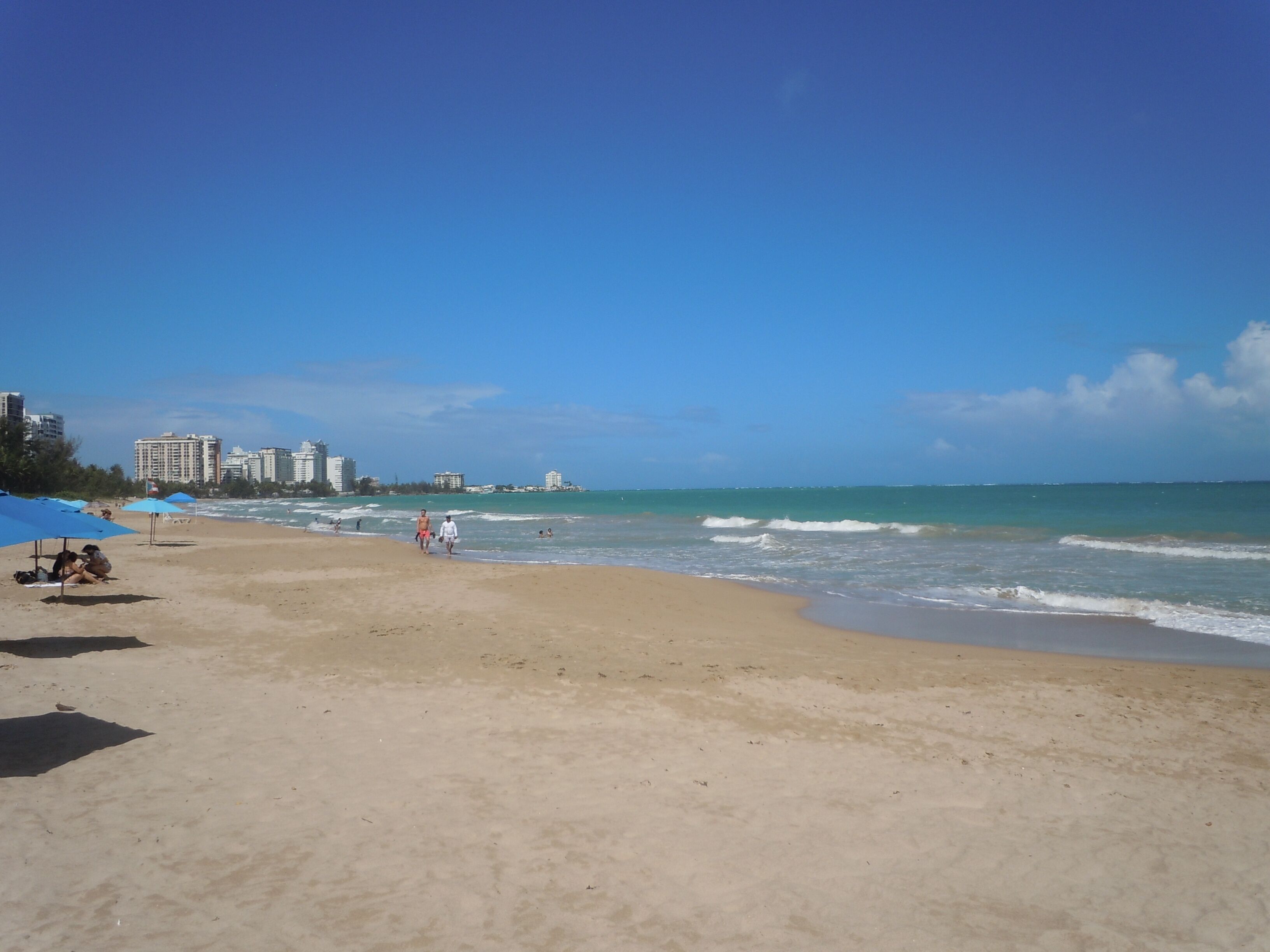 Ein Strand mit Sandküste, Sonnenschirmen und Menschen.