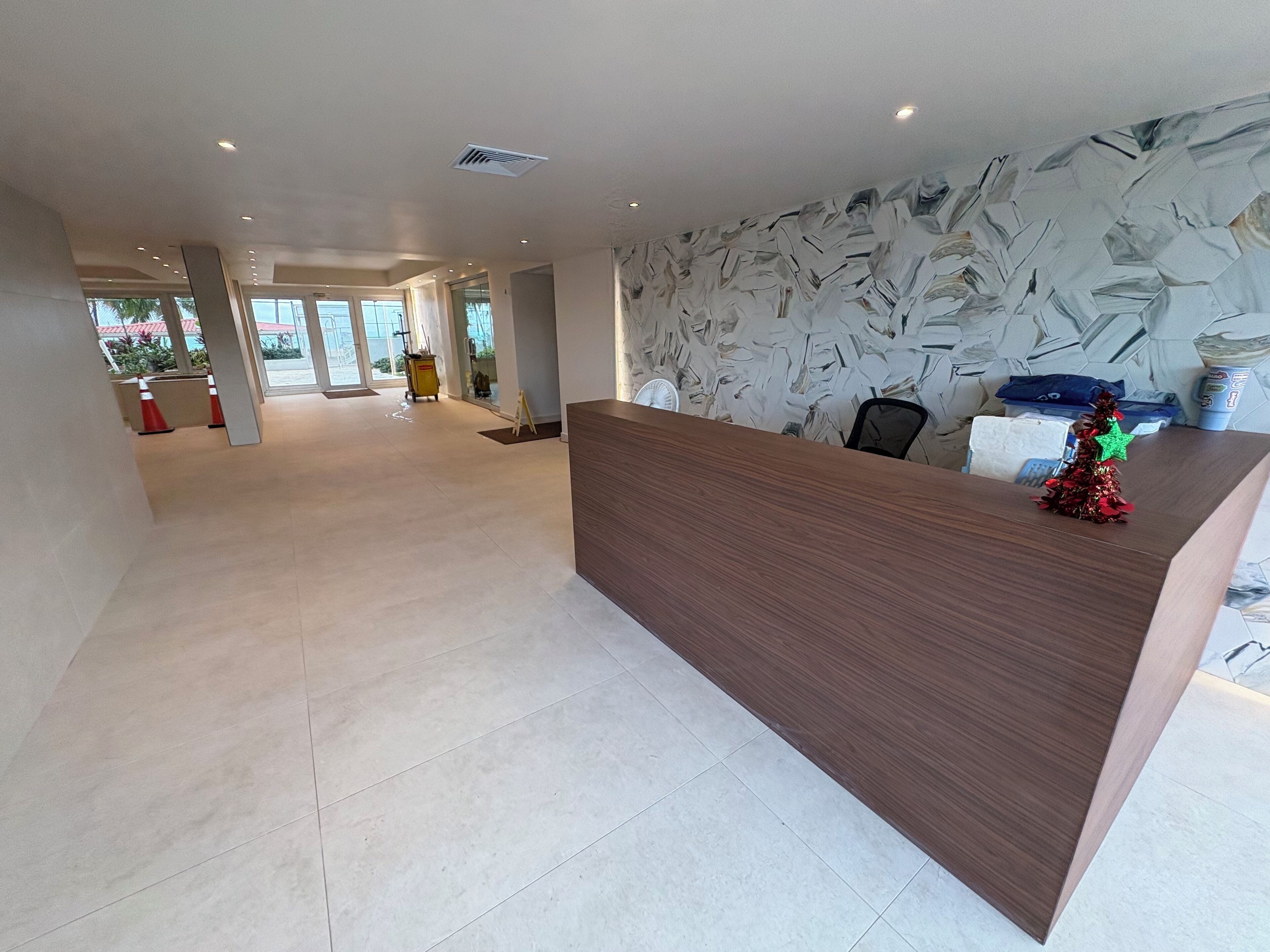 A spacious lobby with a wooden reception desk, a decorative Christmas tree, and a patterned wall.