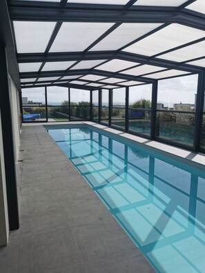 Ein moderner, überdachter Pool mit Glaswänden und freiem Blick auf die umliegende Landschaft.