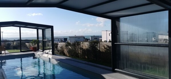 Ein moderner Poolbereich im Freien mit Glasveranda, Blick auf das Meer und blauem Himmel.