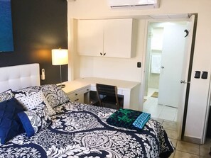 A bedroom with a bed, a desk, and a chair. There is a door leading to a bathroom. - Tropical Oasis in Aruba | Walk to Palm Beach (Noord)