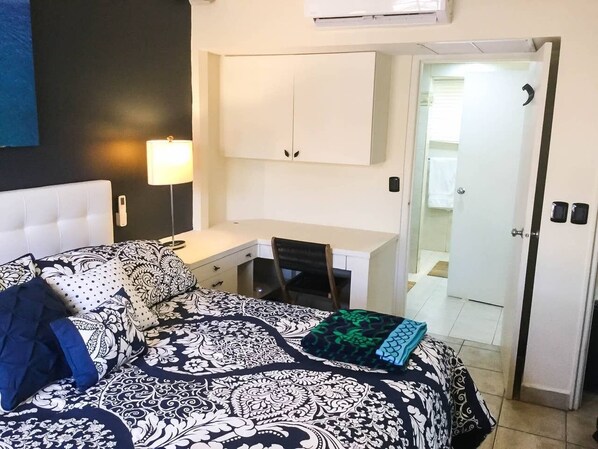A bedroom with a bed, a desk, and a chair. There is a door leading to a bathroom.