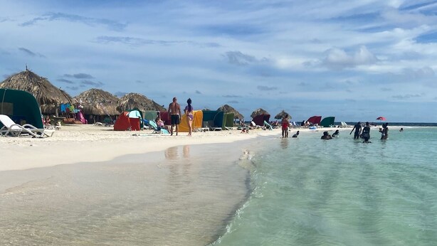 Ein Strand mit klarem, flachem Wasser, Sonnenschirmen und Liegestühlen.