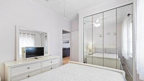 A bedroom with a bed, a dresser, a TV, a mirror, and a walk-in closet. - Quaint Beach Condo with Bay Views, Covered Parking, Pool, Bay Beach -Baywatch C4 (Pensacola Beach)