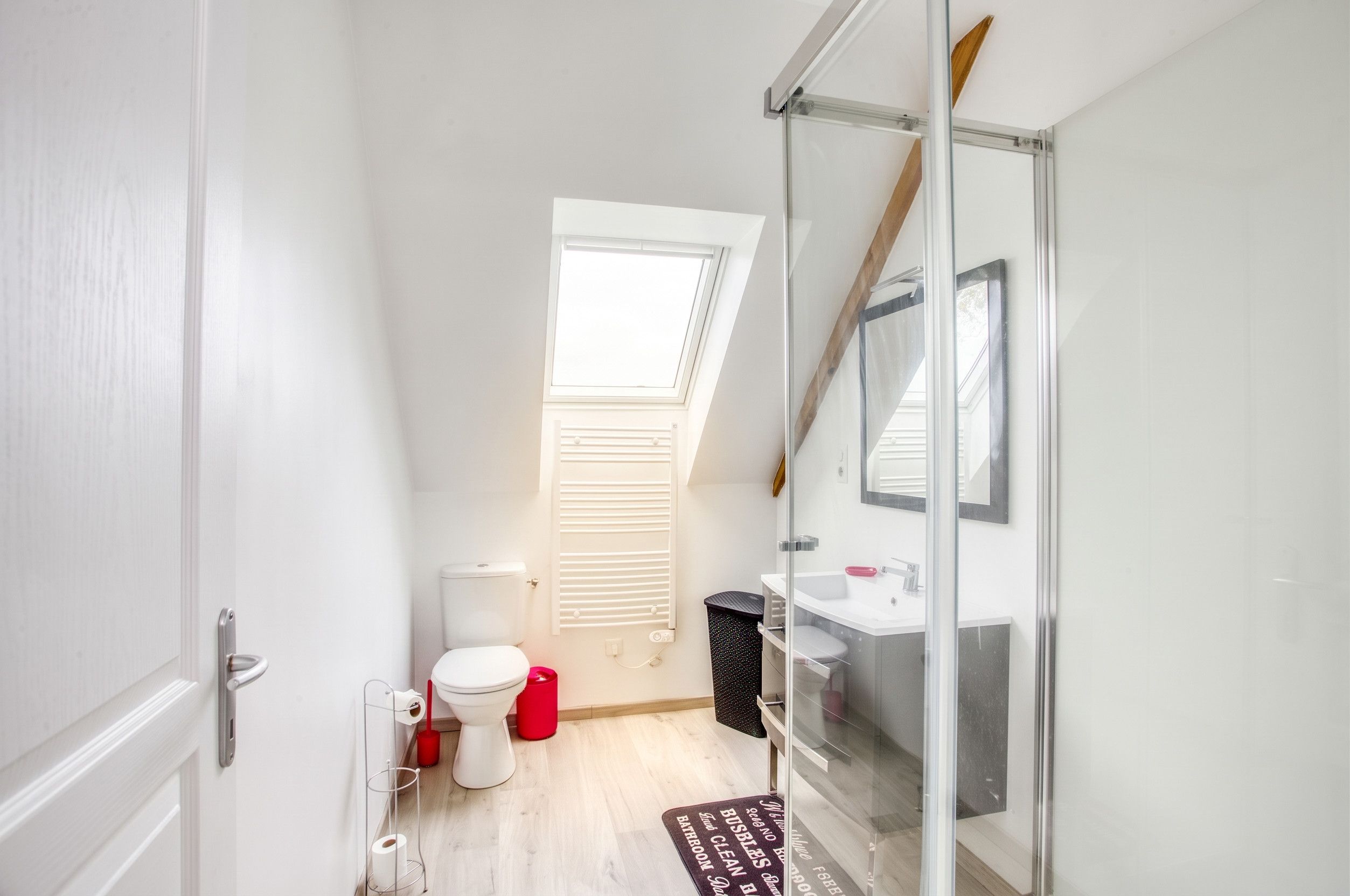 A compact bathroom with a toilet, bidet, and sink. There's a window with blinds, a mirror, and a door.