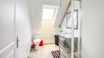 A compact bathroom with a toilet, bidet, and sink. There's a window with blinds, a mirror, and a door.