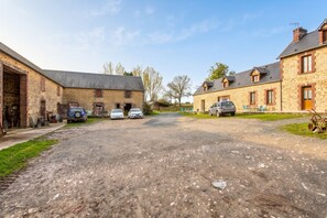A rural street with stone buildings, a gravel road, and parked cars. - Homerez - House Saint-Marcouf (Saint-Marcouf)