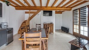 A spacious kitchen with wooden beams, a dining area with a table and chairs, a built-in oven, and a large window with blinds. - Homerez - House Saint-Marcouf (Saint-Marcouf)
