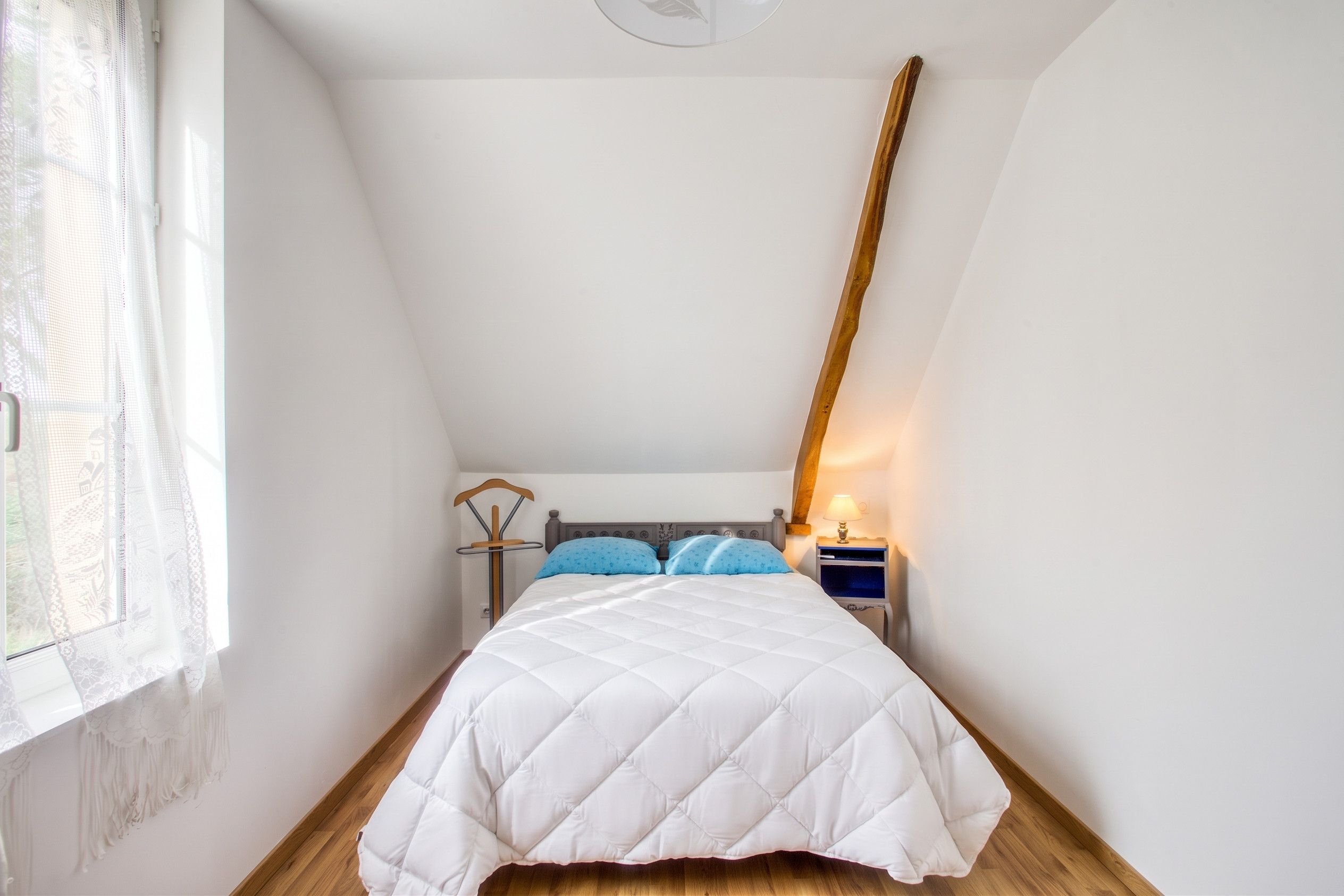 A bedroom with a bed, a nightstand, a lamp, and a window with a curtain.