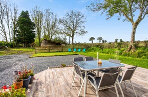 An outdoor patio with a table and chairs, surrounded by a gravel path and a wooden deck. - Homerez - House Saint-Marcouf (Saint-Marcouf)