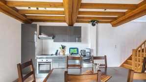 A modern kitchen with stainless steel appliances, wooden beams, and a dining area with a table and chairs. - Homerez - House Saint-Marcouf (Saint-Marcouf)