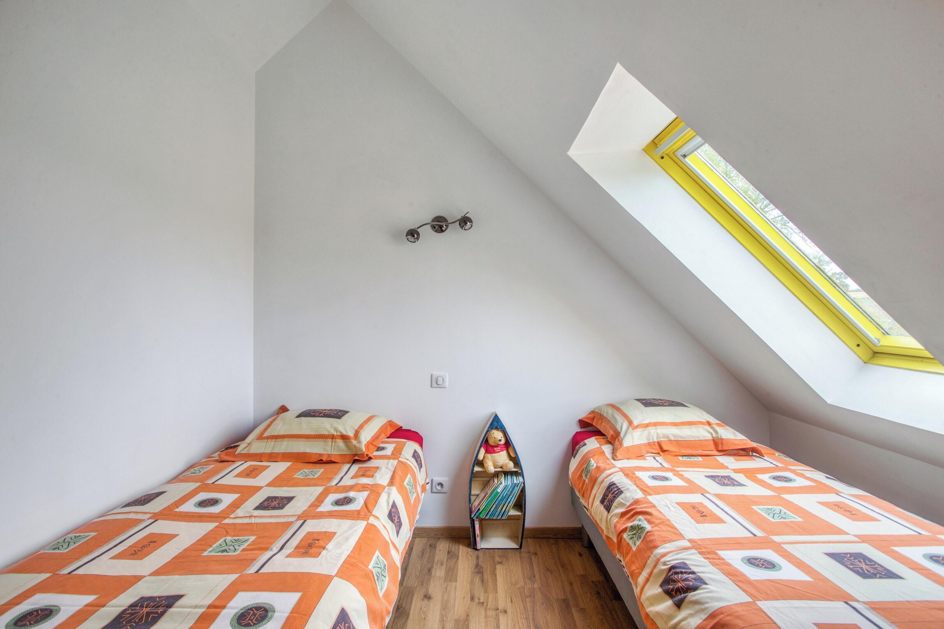 A small, bright room with two beds, a skylight, and a shelf unit.