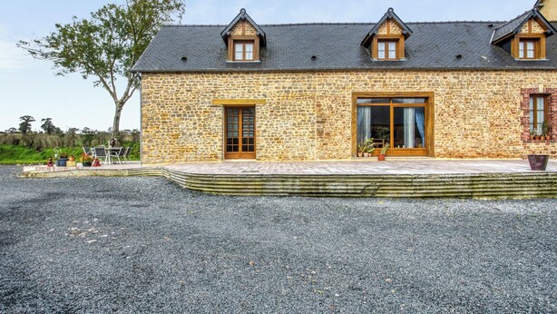 A stone building with a sloped roof, a large glass door, and a small porch area. - Homerez - House Saint-Marcouf (Saint-Marcouf)