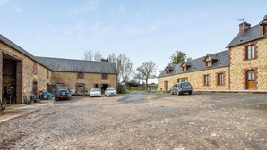 A gravel driveway leading to a row of stone buildings with parked cars. - Homerez - House Saint-Marcouf (Saint-Marcouf)