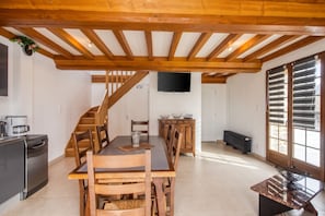 A dining area with a wooden table, chairs, a coffee machine, and a TV mounted on the wall. - Homerez - House Saint-Marcouf (Saint-Marcouf)