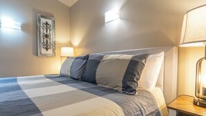Un letto rifatto con una coperta a quadri, una lampada da comodino e un punto luce a parete.