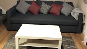 Un salon avec un canapé gris foncé, une table basse blanche et un tableau représentant un paysage urbain accroché au mur.