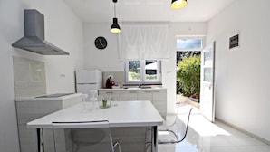 A modern kitchen with white cabinetry, a stainless steel range hood, and a dining area with a white table and chairs. - Luxury Apartments Gold and Grey (Zadar)