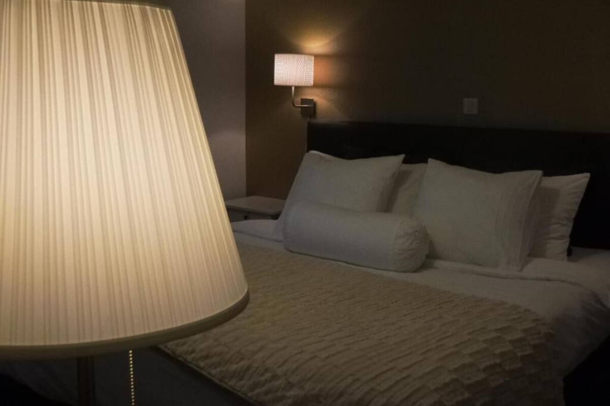 A hotel room with a large floor lamp, a bed with white bedding, and a wall-mounted light fixture.