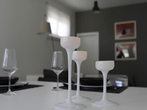 A dining table with three white wine glasses and a small white cup, set against a neutral-toned wall with framed pictures.