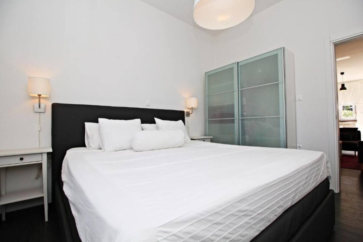 A modern hotel room with a large bed, white bedding, and a glass cabinet.