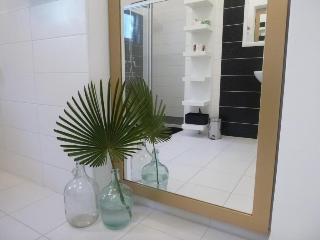 A bathroom with white tiles, a large mirror, and a potted plant.