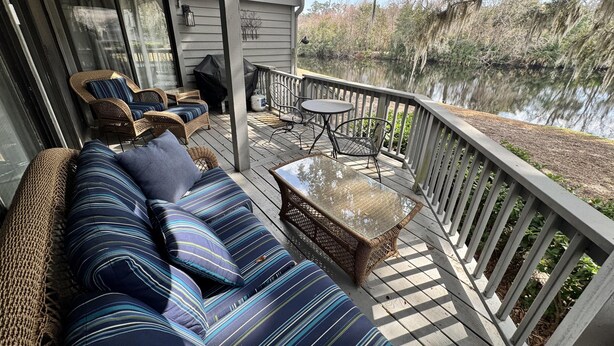 A covered deck with a sofa, chairs, and a table, overlooking a body of water. - Completely Updated Luxury Villa in Sea Pines - Beautiful Lagoon View. (Hilton Head Island)