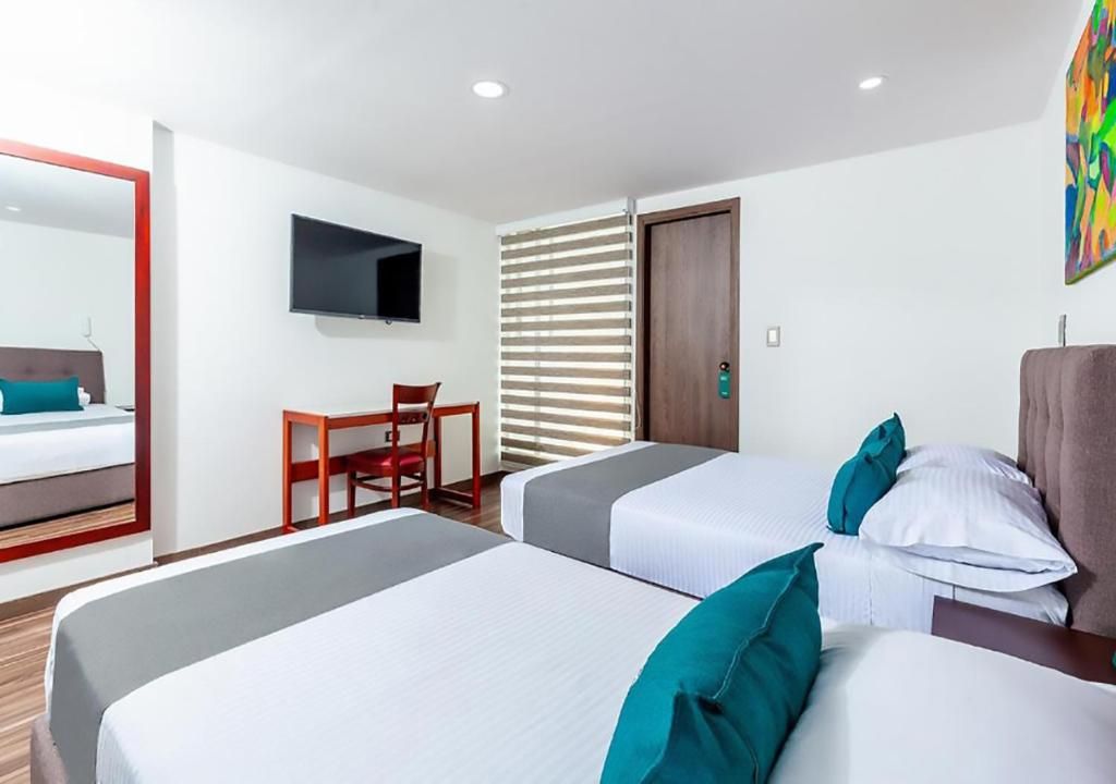 A hotel room with two beds, a desk, a chair, a TV, and a door with blinds.
