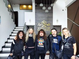 A group of people standing in front of a hotel sign with a staircase in the background.
